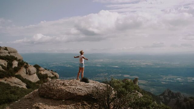 Shot of female hiker on top of Montserrat mountain in Spain. Traveler woman with arms raised looking at the view. 