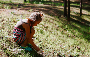 The child is squatting. Baby girl in a striped dress outdoors. Rest in the park. Copy space.