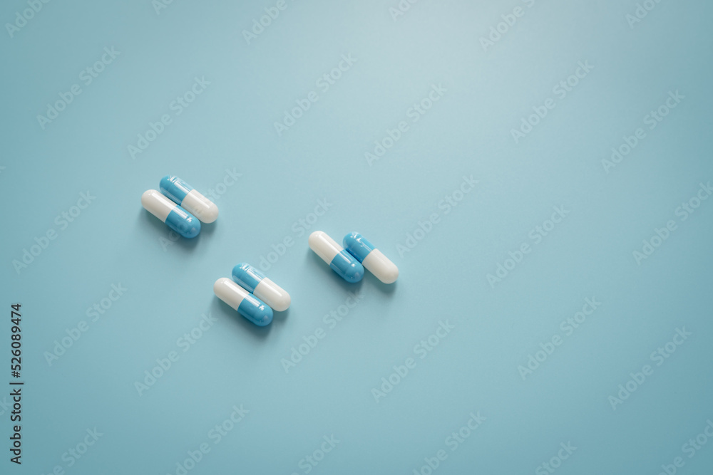 Poster Pairs of white-blue antibiotic capsule pills on blue background. Antibiotic drug. Prescription drug. Pharmacology and recommended dose concept. Pharmaceutical industry. Medical and healthcare concept.