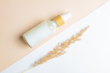White Cream bottle and dry reed grass on pastel background. Cosmetic skincare product blank frosted glass package. White bottle of unbranded lotion, balsam, hand creme mockup, flat lay.