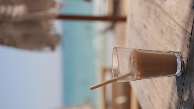 Ice coffee latte in tall glass with straw by the sea in beach bar
