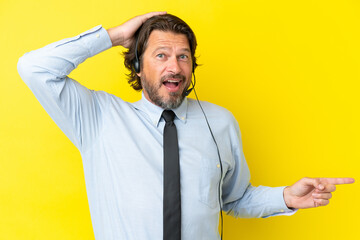 Telemarketer dutch man working with a headset isolated on yellow background surprised and pointing finger to the side