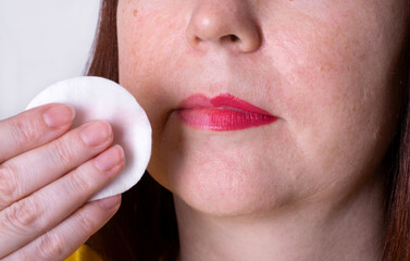 Wiping lipstick with make-up remover pad. Cleansing skincare routine. Close-up of mature adult woman lips