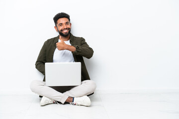 Young Brazilian man with a laptop sitting on the floor isolated on white giving a thumbs up gesture