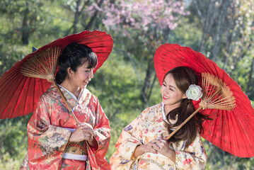 Two young Asian women wearing traditional japanese kimono and red umbrella in the sakura blossoms...