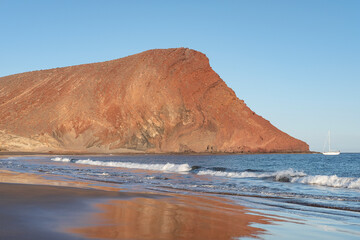 View of Montana Roja, a red stratovolcano, and its reflection in the sand of Playa la Tejita, soft afternoon light elevating the striking colors of the volcanic cone, Tenerife, Canary islands, Spain