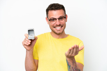 Young caucasian man holding a engagement ring isolated on white background inviting to come with hand. Happy that you came