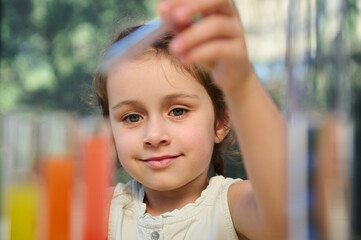 Close-up. Beautiful Caucasian schoolgirl, little chemist making chemical scientific experiments while learning chemistry. Blurred test tubes with colorful reagents on the foreground. Back to school