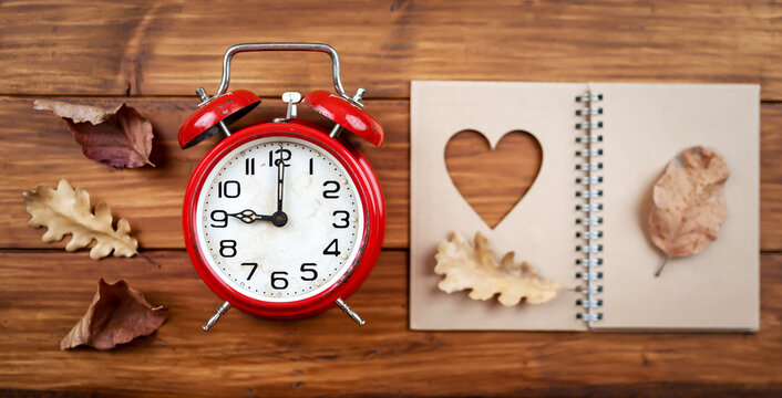 Alarm clock with autumn leaves and love heart book. Daylight savings time, fall banner, background.