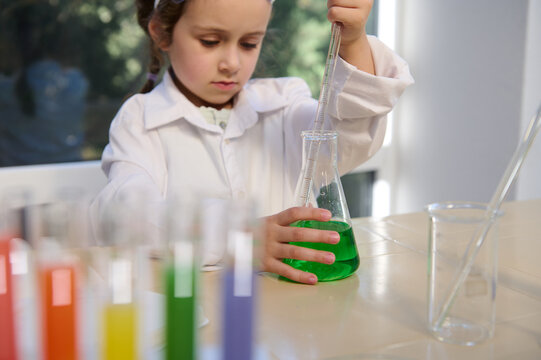 Selective focus on flat-bottomed flask with green liquid and little girl's hand holding pipette, collecting some chemicals, doing science experiments in school lab during chemistry lesson