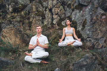 Naklejka na ściany i meble a young couple meditates sitting in a lotus position on a rock.