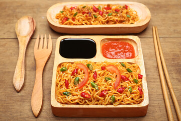 Instant fried noodles with soy sauce and spicy chili sauce in bowl on wooden table background. Top view.