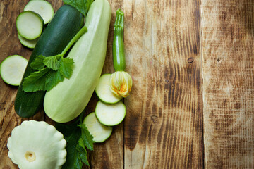 The raw product of zucchini and patissons lie on the wooden surface of the table. Ingredients for cooking. Seasonal vegetables.