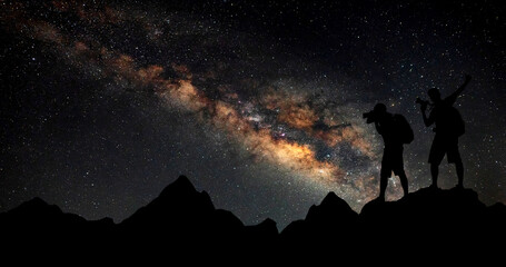 Silhouette of Two Cameraman standing on rock.Warm Color night sky with stars and milky way with man on the mountain. High Rocks.Background with galaxy and silhouette of a man. Many stars.