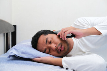 Fototapeta na wymiar Side view of Asian man answering a phone call until he sleeping