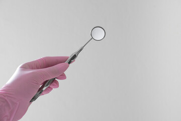 Hand mit rosa Handschuh hält Mundspiegel für die Zahnmedizin auf weißen Hintergrund
