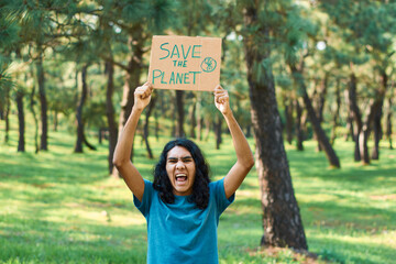 Young teenage man holding sign that says SAVE THE PLANET, in the forest.