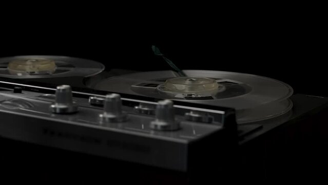 A vintage 1970s open-reel quarter-inch audio tape recorder spooling with record button depressed. Subdued lighting suggesting covert recording, wiretap, or espionage.