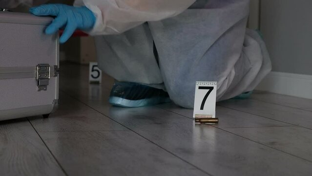 Forensic expert criminologist collects evidence at  crime scene, packaging of  fired cartridge case from  firearm, gloved hands close-up