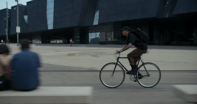 Young handsome man commute to work or school on minimalistic city bike. Student or office worker on way to university or office ride bike on bike lane. Pedalling and riding bike. Cycling in the city - Powered by Adobe