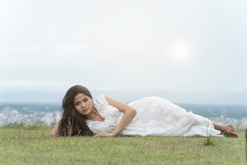 woman half sitting,half lying on grass at top mountian look at camera,sky,city and nature view...