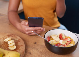 A young woman looks at her cellphone while eating healthy breakfast