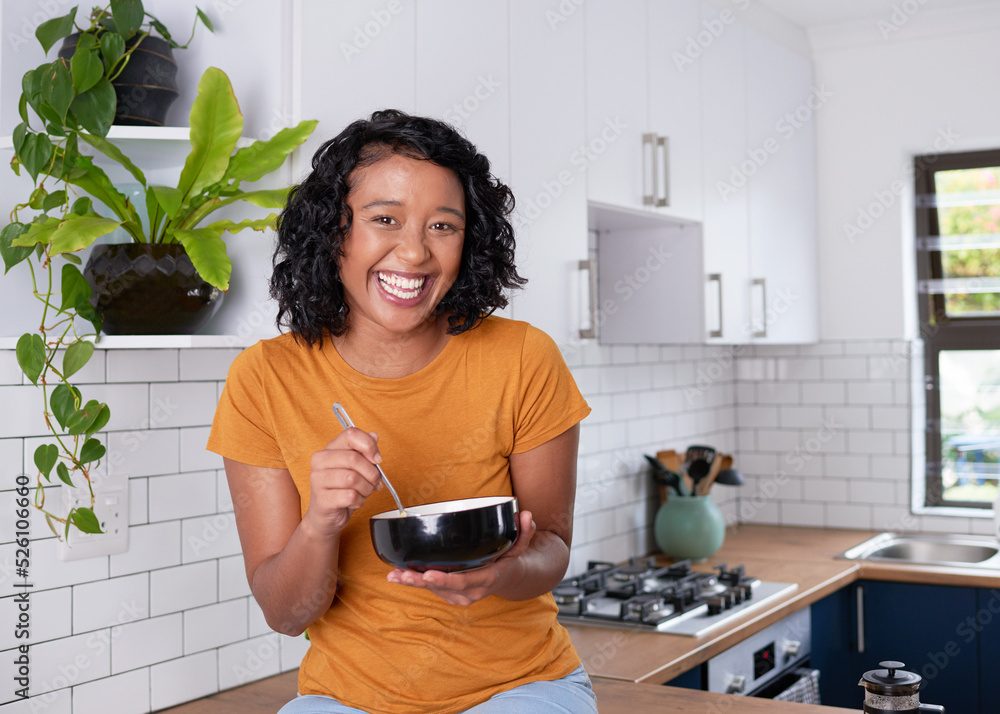 Wall mural A young multi-ethnic woman sits on her kitchen counter eating breakfast