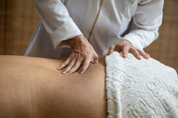 Um profissional fazendo massagem terapêutica nas costas do paciente que está deitado na maca. - obrazy, fototapety, plakaty