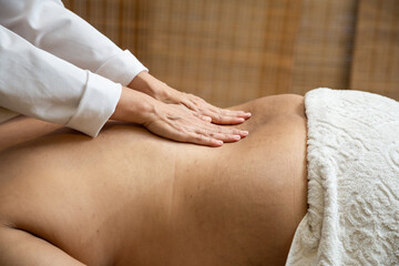 Um profissional fazendo massagem terapêutica nas costas do paciente que está deitado na maca. - obrazy, fototapety, plakaty