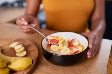 A close up of young woman eating bowl of cornflakes with fruit for breakfast