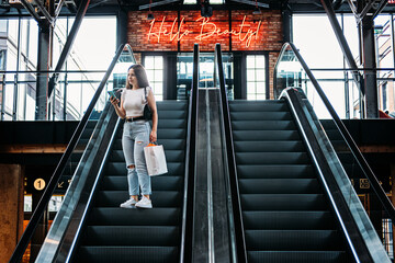 Young brunette Latina attractive woman with shopping bags on escalator in the fashion store mall.