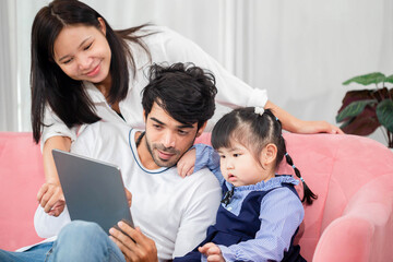 Family spending time on a sofa in the living room, Parents and daughter using digital tablet at home, Young family with child having fun using modern technology