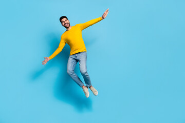 Fototapeta na wymiar Full body portrait of active excited man hands wings jumping flight isolated on blue color background