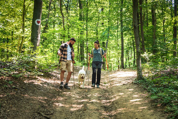 Obraz premium Young happy couple and their dog at hiking through the woods enjoying the sight. Two nature lovers in the mountain forest enjoy healthy walking through the nature. With film grain selective focus
