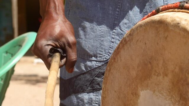 Slow motion footage of black man playing Dunun drum, focus on the hand holding the wooden stick