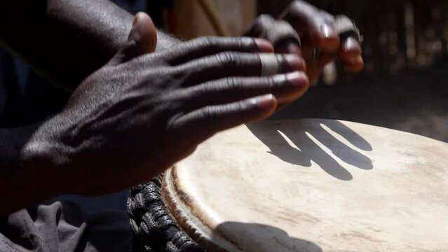 Slow motion footage of black hands playing djembe from the side