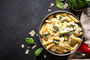 Pasta penne with chicken and spinach in creamy sauceon black table. Top view with copy space.