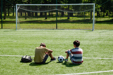 Teenagers talking in school stadium outdoors. Teenage boy comforting consoling upset sad friend. Education, bullying, conflict, problems at school, lost game, learning difficulties, empathy concept - obrazy, fototapety, plakaty