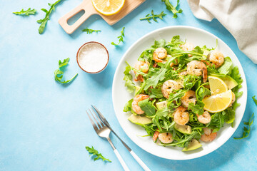 Shrimp salad with arugula and avocado at blue table. Top view with space for text.