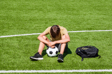 Sad alone teenage boy sitting in empty school sport stadium outdoors. Emotions, defeat, lost game,...