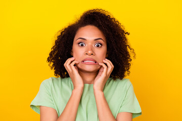 Photo of impressed scared girl dressed green t-shirt arms cheeks big eyes isolated yellow color background