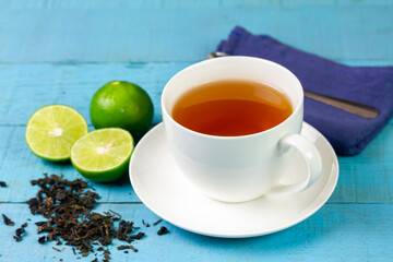 Hot tea in white cup with fresh lime on blue wooden background.