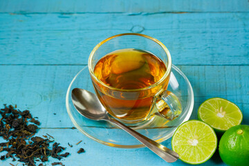 Hot tea in glass cup with fresh lime on blue wooden background.