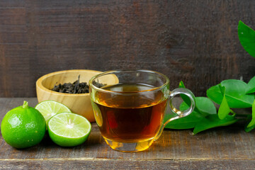 Hot tea in glass cup with fresh lime and leaf on rustic wooden background.