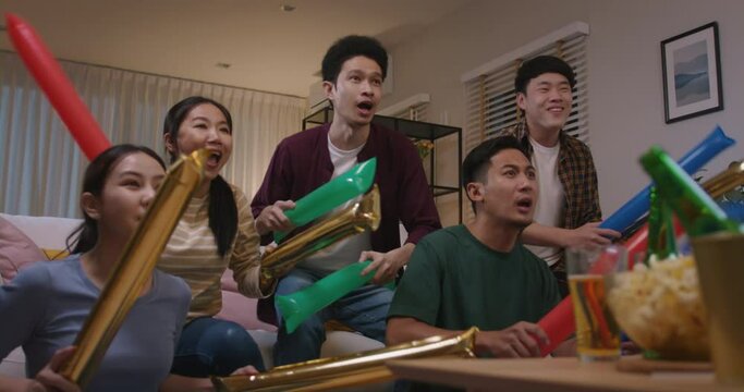 Group of young adult friend man and woman asia people sit at sofa couch joy night party fun game FIFA world cup live TV at home eat snack bowl drink beer bottle glass jump mad happy win exult face.