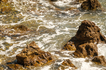 Small ocean waves crashing of rocks on shallow coastline at high tide at bright sunlight....