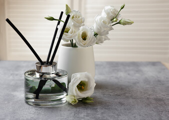 Reed diffuser and vase with eustoma flowers on gray marble table, space for text