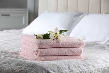 Stack of clean towels and lily flowers on bed indoors