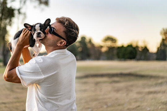 Handsome young man holding up and kissing a french bulldog.