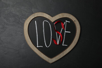 Heart shaped blackboard with word LOVE and letter S of red ribbon on dark background, top view. Composition symbolizing problems in relationship